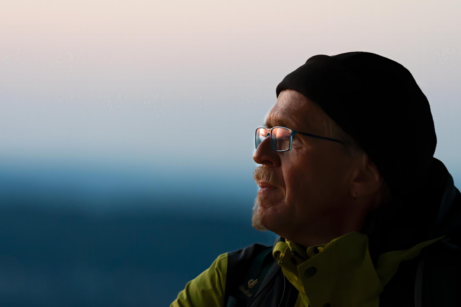 Profilporträt eines älteren Mannes mit Mütze und Brille in der Abenddämmerung