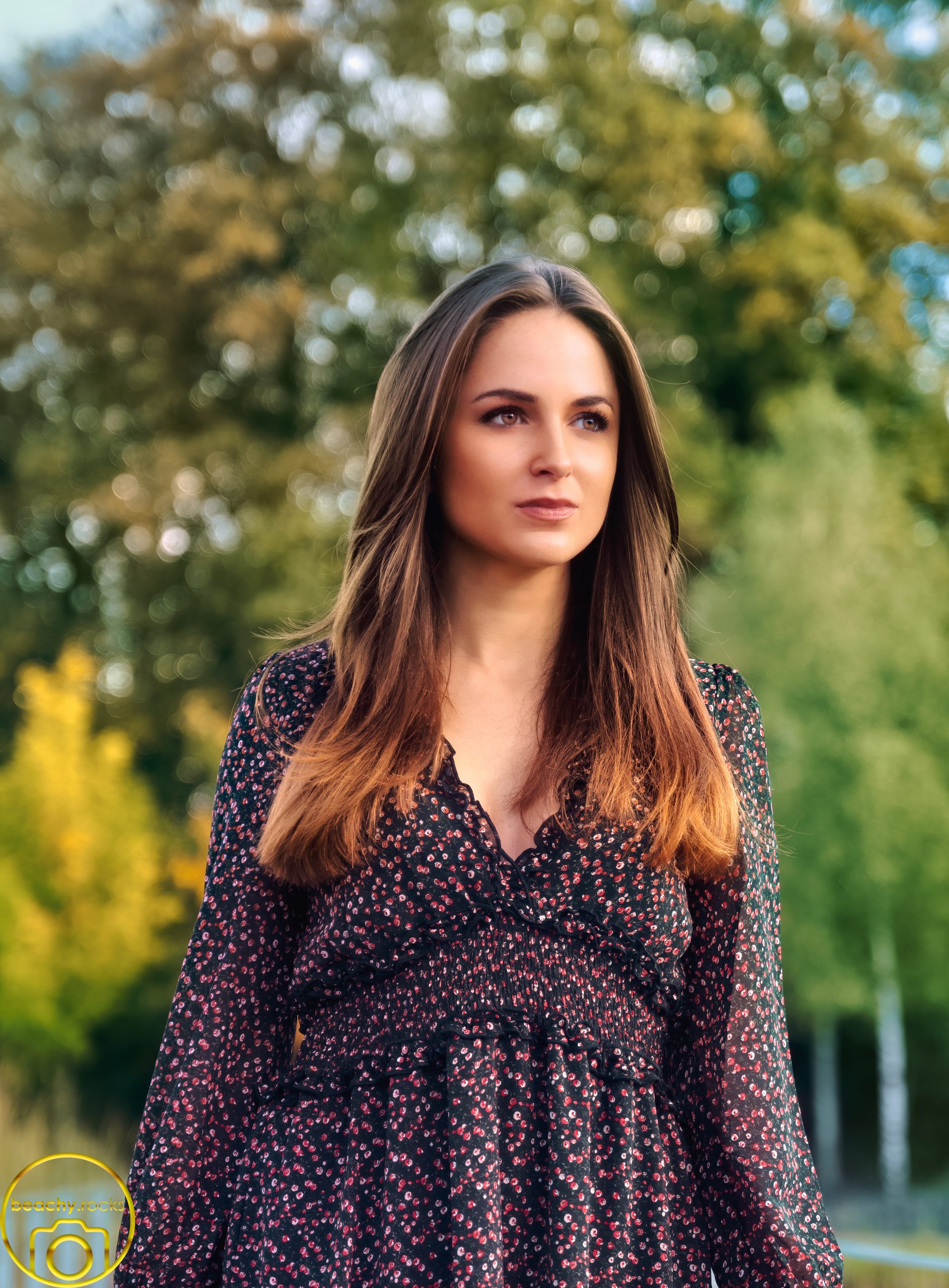 Frau mit langen Haaren im geblümten Kleid vor herbstlichen Bäumen